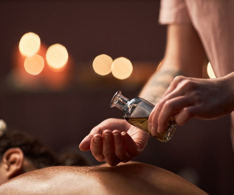 Massage aux Huiles Relaxantes : Soin et Bien-être au Spa Thérapeute verse de l'huile de massage sur sa main pour un soin relaxant dans un spa à l'ambiance tamisée.